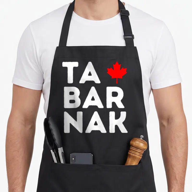 Tablier de cuisine noir avec l'inscription TABARNAK en blanc et une feuille d'érable rouge stylisée sur la partie supérieure.