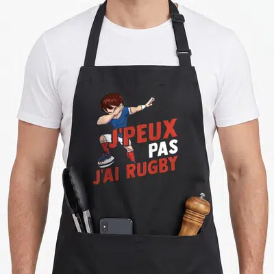 Tablier de cuisine noir avec un garçon effectuant un dab et le texte j'peux pas j'ai rugby imprimé en rouge et blanc.