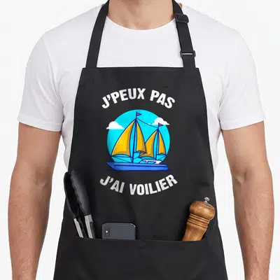 Tablier de cuisine noir avec illustration d'un voilier jaune et bleu et le texte j'peux pas j'ai voilier en blanc.