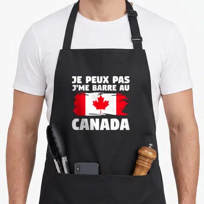 Tablier de cuisine noir avec le texte Je peux pas j'me barre au Canada et un drapeau canadien stylisé.