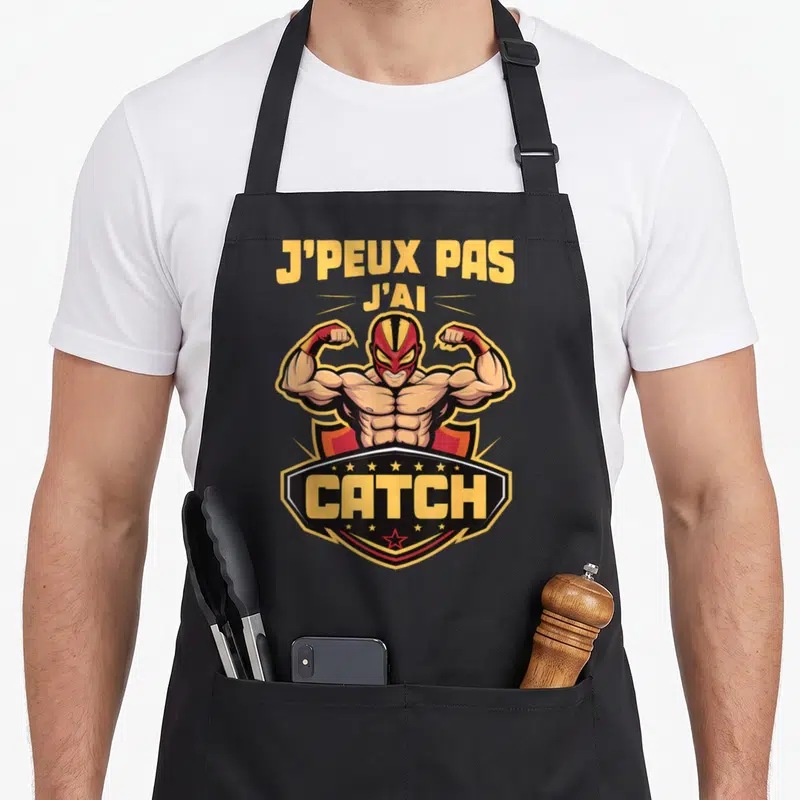 Tablier de cuisine noir avec un luchador musclé et le texte J'peux pas j'ai catch imprimé en jaune.
