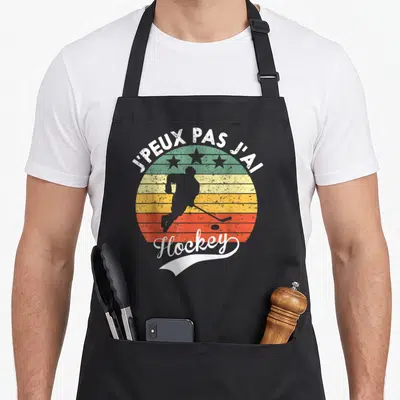Tablier de cuisine noir avec motif vintage montrant un joueur de hockey sur fond rayé multicolore et texte blanc.