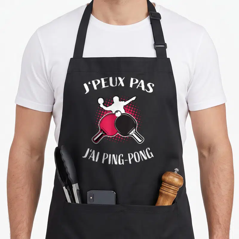 Tablier de cuisine noir avec deux raquettes de ping-pong rouge et noire croisées et une silhouette blanche jouant.