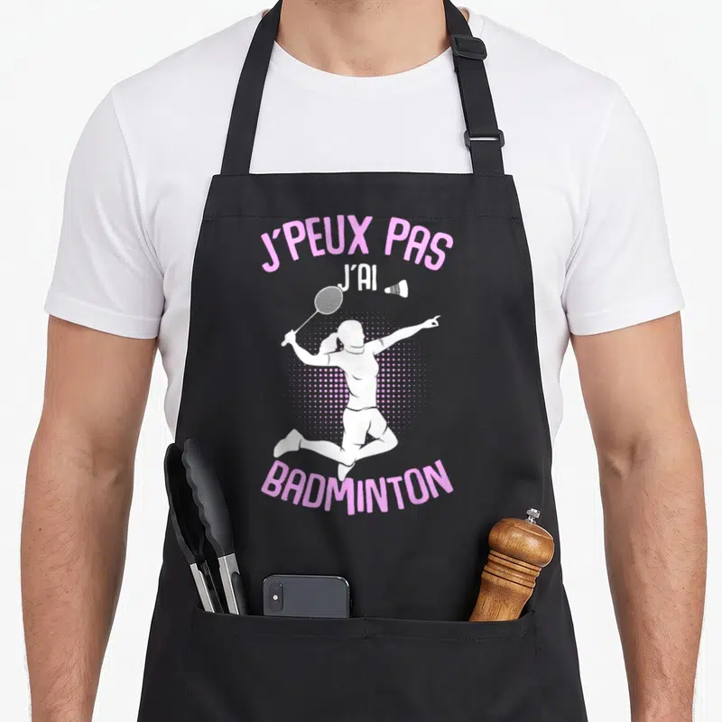 Tablier de cuisine noir avec silhouette blanche de joueuse de badminton et texte rose J'PEUX PAS J'AI BADMINTON