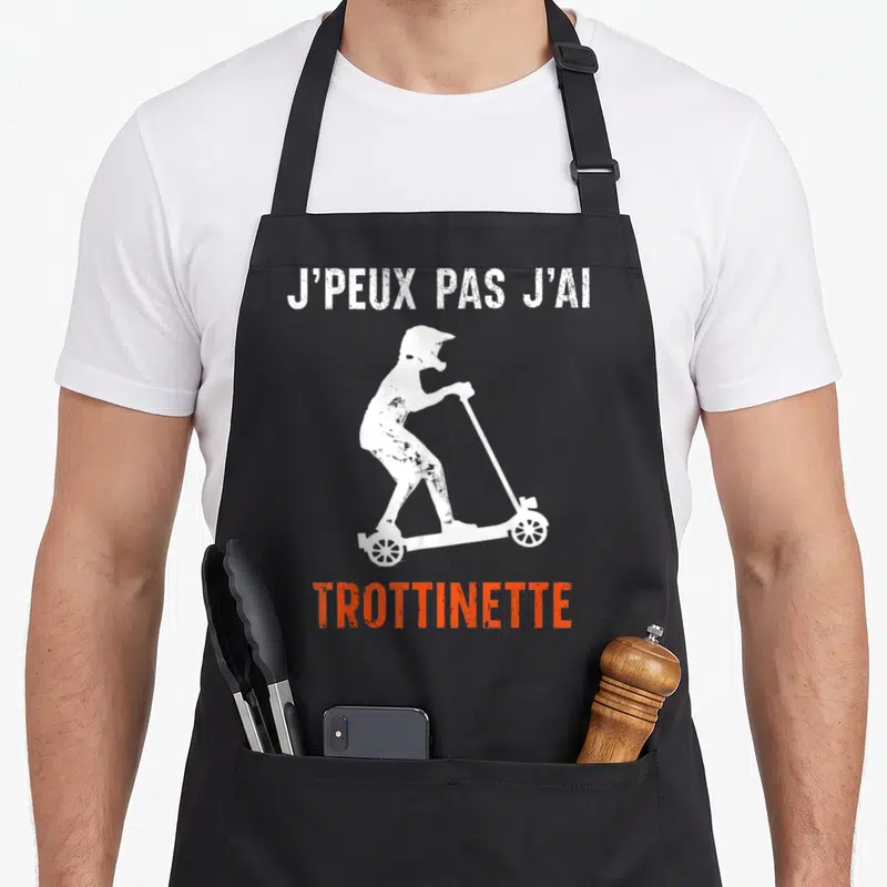 Tablier de cuisine noir avec silhouette blanche d'un rider en casque sur trottinette et texte j'peux pas j'ai trottinette en blanc et orange.