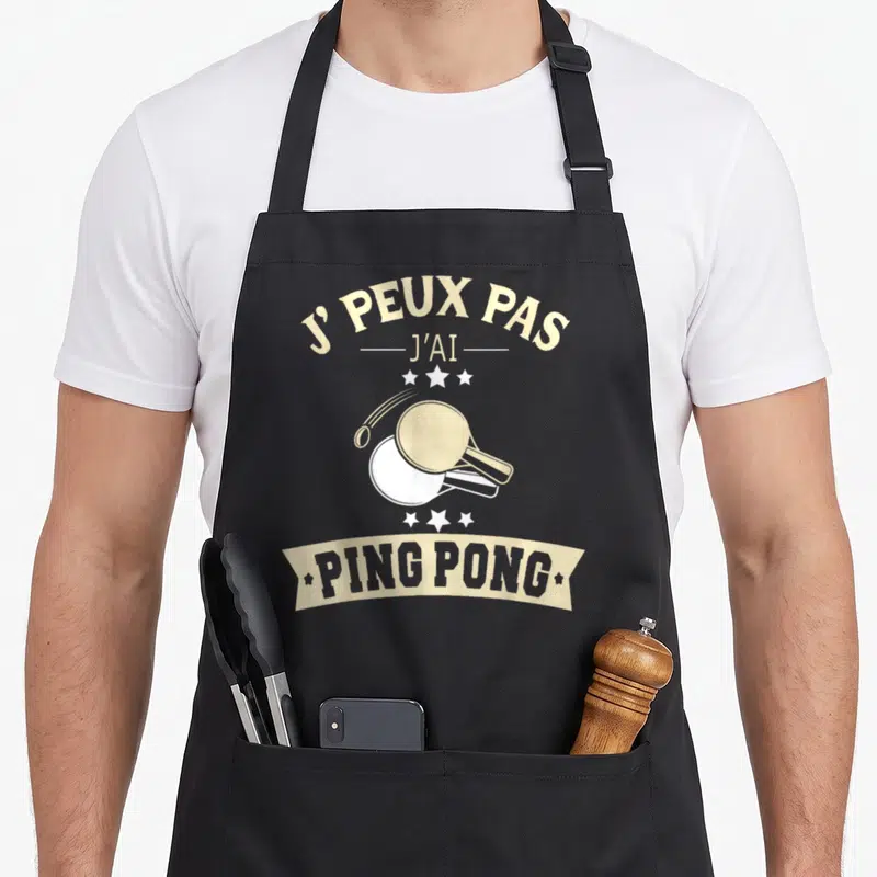 Tablier de cuisine noir avec inscription j'peux pas j'ai ping pong illustré par une raie et une balle blanche.