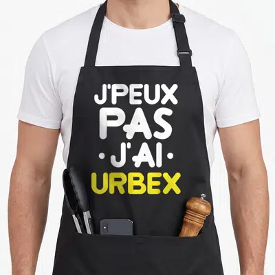 Tablier de cuisine noir avec l'inscription j'peux pas j'ai urbex en blanc et jaune.