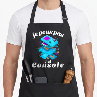 Tablier de cuisine noir avec illustration de console bleue éclatée et texte je peux pas j'ai console en blanc.