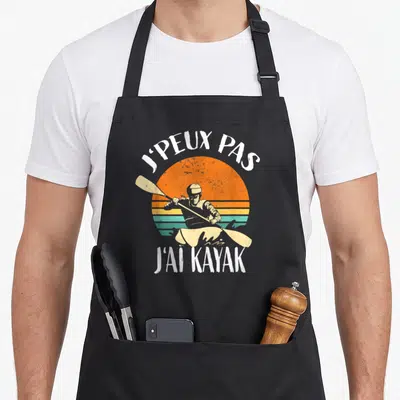 Tablier de cuisine noir avec illustration vintage d'un kayakiste devant un soleil orange et la citation J'PEUX PAS J'AI KAYAK