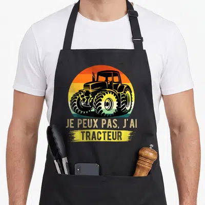 Tablier de cuisine noir avec illustration de tracteur noir sur fond dégradé orange et jaune, texte je peux pas j'ai tracteur