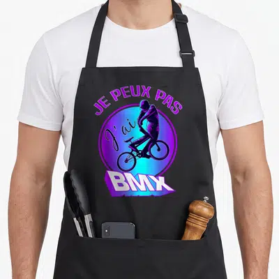 Tablier de cuisine noir avec un cycliste BMX violet et le texte Je Peux Pas J'ai BMX en lettres colorées.