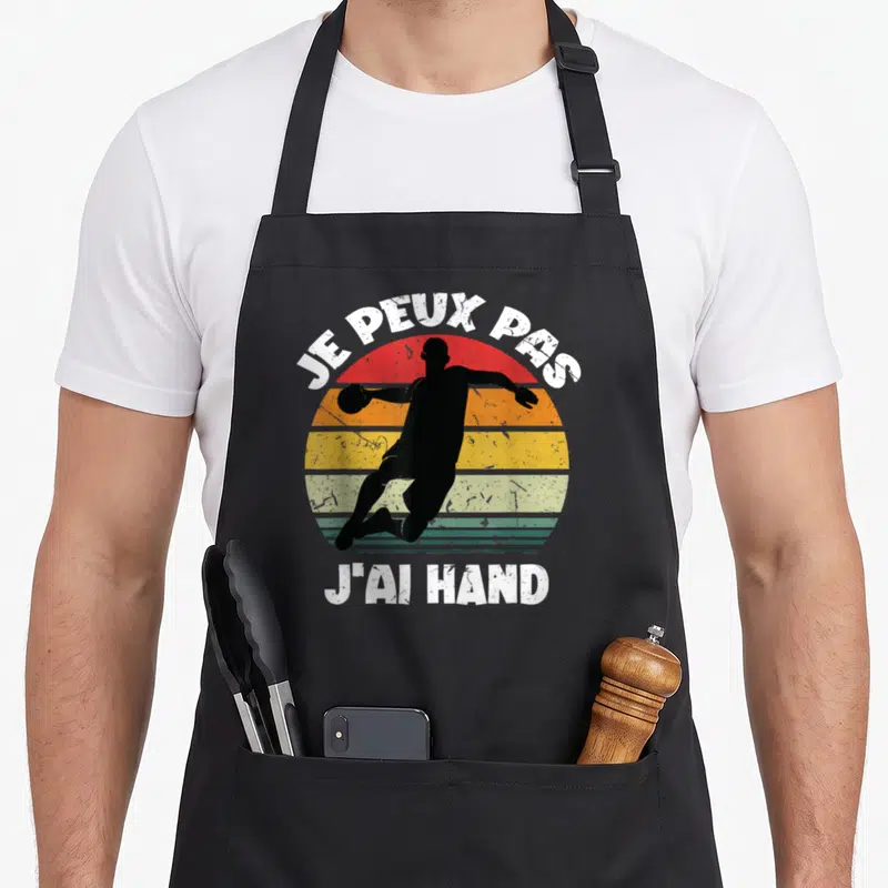 Tablier de cuisine noir avec silhouette de handballeur et texte je peux pas j'ai hand sur fond coloré vintage.