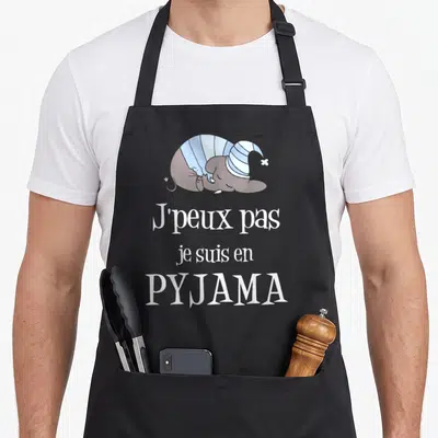 Tablier de cuisine noir avec un éléphant dormant en pyjama et le texte J'peux pas je suis en pyjama imprimé en blanc.