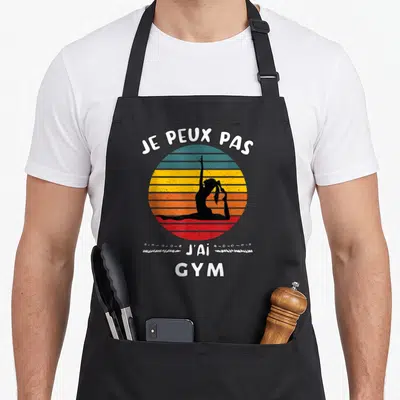 Tablier de cuisine noir avec silhouette de gymnaste et texte je peux pas j'ai gym sur fond de soleil coloré.