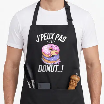 Tablier de cuisine noir avec illustration de deux donuts colorés et texte blanc humoristique sur fond uni.