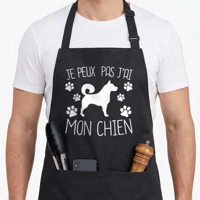 Tablier de cuisine noir avec silhouette de chien blanc, traces de pattes et texte Je peux pas j'ai mon chien.