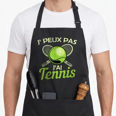 Tablier de cuisine noir avec une balle de tennis verte et deux raquettes croisées en arrière-plan.