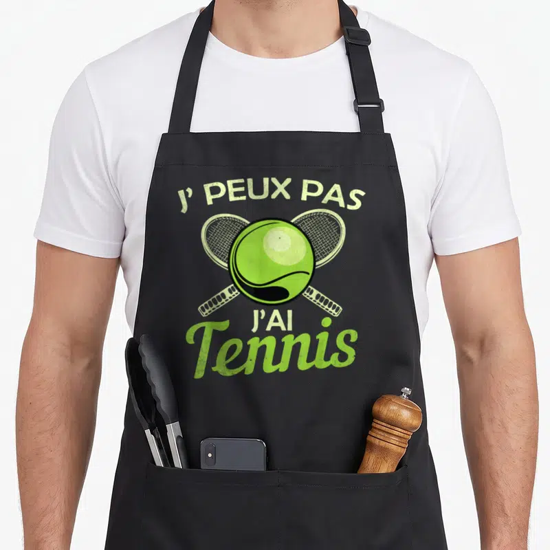 Tablier de cuisine noir avec une balle de tennis verte et deux raquettes croisées en arrière-plan.