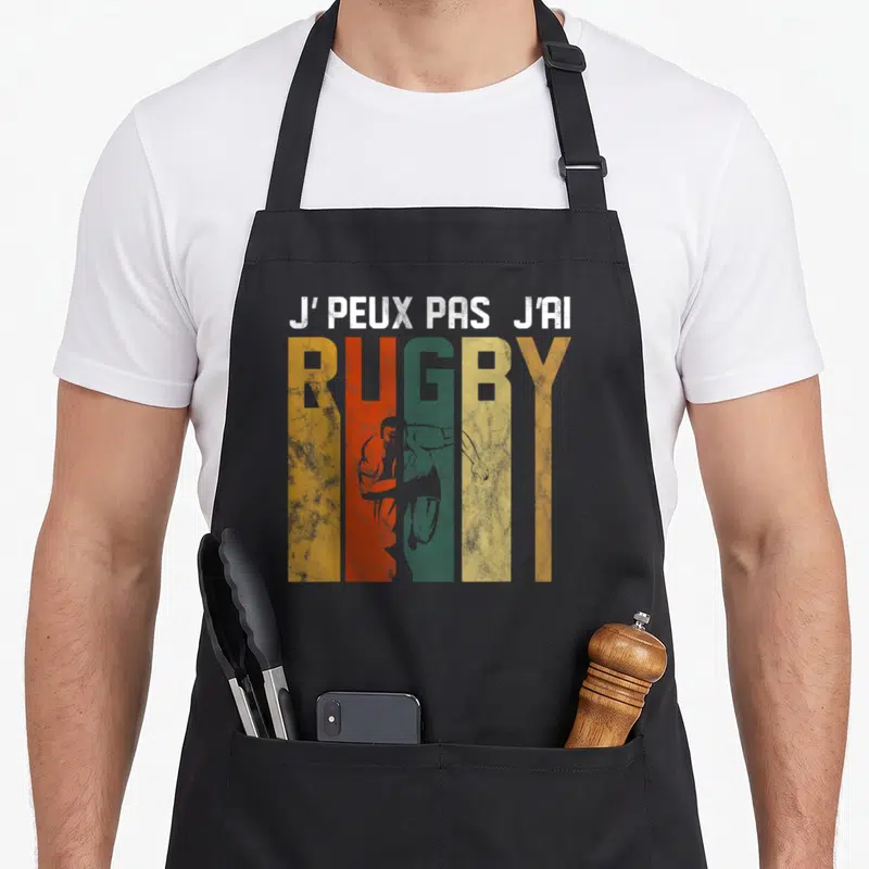 Tablier de cuisine noir avec inscription j peux pas j ai rugby et silhouette de joueur dans des lettres colorées.