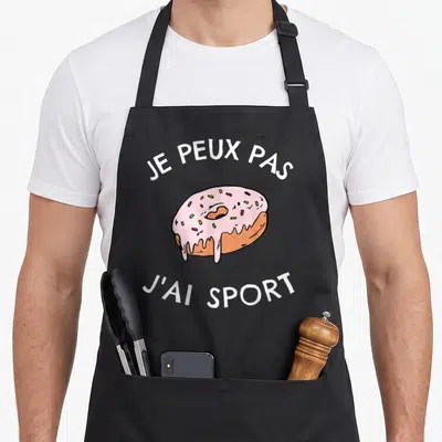 Tablier de cuisine noir avec un donut rose glacé et la phrase je peux pas j'ai sport imprimée en blanc.