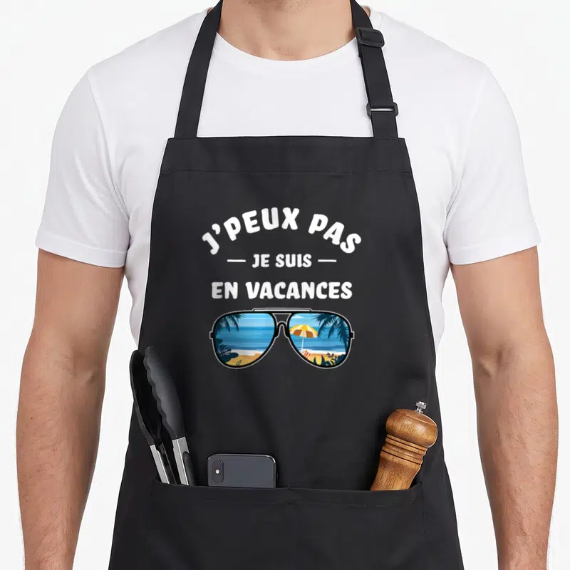 Tablier de cuisine noir avec inscription j'peux pas je suis en vacances au-dessus d'une illustration de lunettes de soleil.