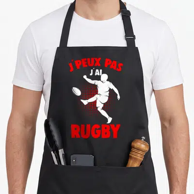 Tablier de cuisine noir avec silhouette blanche de joueur de rugby et texte rouge J'peux pas j'ai rugby.