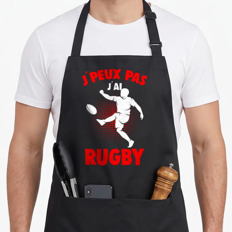 Tablier de cuisine noir avec silhouette blanche de joueur de rugby et texte rouge J'peux pas j'ai rugby.