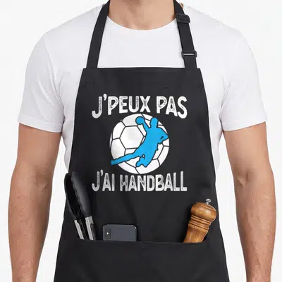 Tablier de cuisine noir avec silhouette handballeur bleue sur balle blanche et texte blanc déstructuré.