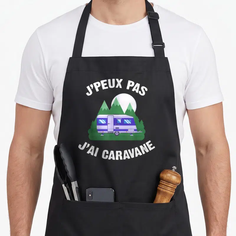 Tablier de cuisine noir avec illustration d'une caravane bleue sous des montagnes et le texte j'peux pas j'ai caravane.