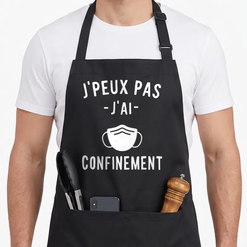 Tablier de cuisine noir avec le texte j'peux pas j'ai confinement et un dessin de masque chirurgical blanc au centre.