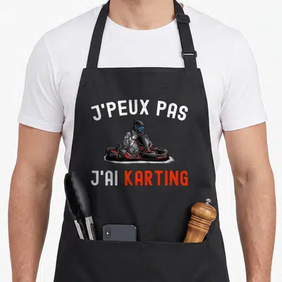 Tablier de cuisine noir avec illustration d'un pilote de karting et le texte j'peux pas j'ai karting imprimé en blanc et orange.