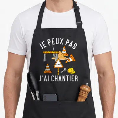 Tablier de cuisine noir avec illustration de barrière, cônes orange, casque jaune et texte Je peux pas j'ai chantier.