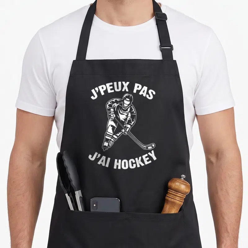 Tablier de cuisine noir avec illustration blanche d'un joueur de hockey sur glace tenant sa crosse et un disque.