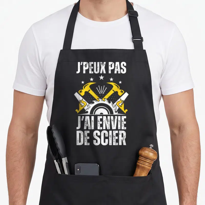 Tablier de cuisine noir avec inscription j'peux pas j'ai envie de scier et outils de bricolage jaunes et blancs.
