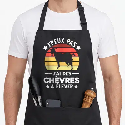 Tablier de cuisine noir avec un soleil rétro, une chèvre grise et le texte j'peux pas j'ai des chèvres à élever en blanc.