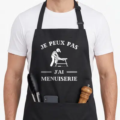 Tablier de cuisine noir avec inscription je peux pas j'ai menuiserie et silhouette d'ouvrier en train de travailler.