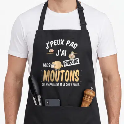 Tablier de cuisine noir avec inscription blanche et orange illustrée de trois moutons cartoon.