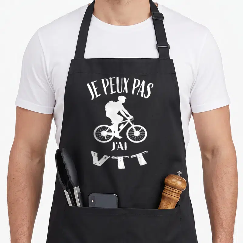 Tablier de cuisine noir avec silhouette blanche de cycliste VTT et le texte je peux pas j'ai VTT imprimé en haut et en bas.