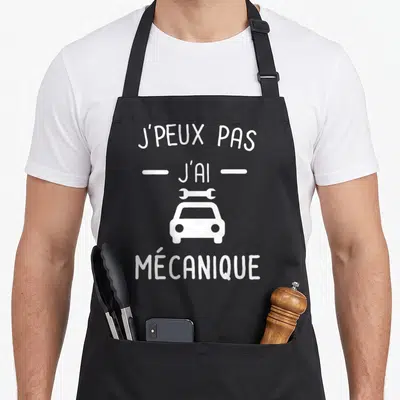 Tablier de cuisine noir avec le texte j'peux pas j'ai mécanique et une illustration de voiture blanche surmontée d'un outil.