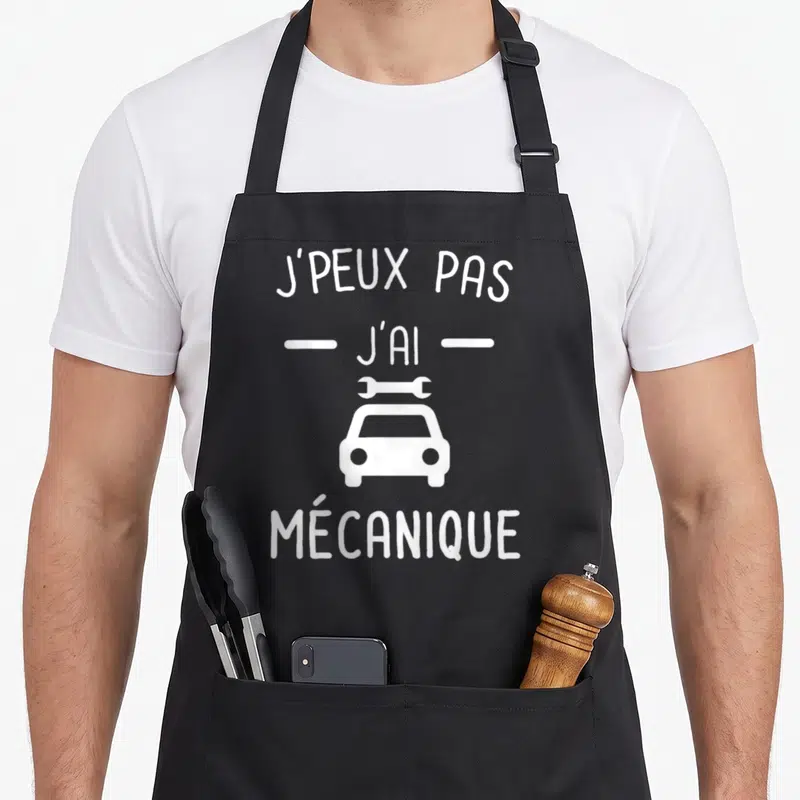Tablier de cuisine noir avec le texte j'peux pas j'ai mécanique et une illustration de voiture blanche surmontée d'un outil.