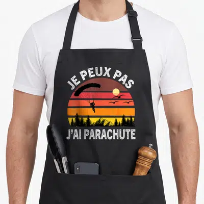 Tablier de cuisine noir avec illustration retro de parachutiste et texte je peux pas j'ai parachute imprimé en blanc.