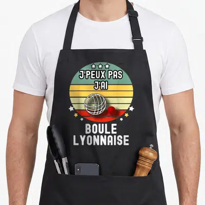 Tablier de cuisine noir avec motif circulaire rétro affichant une boule et une balle rouge sous le texte j'peux pas j'ai boule lyonnaise.