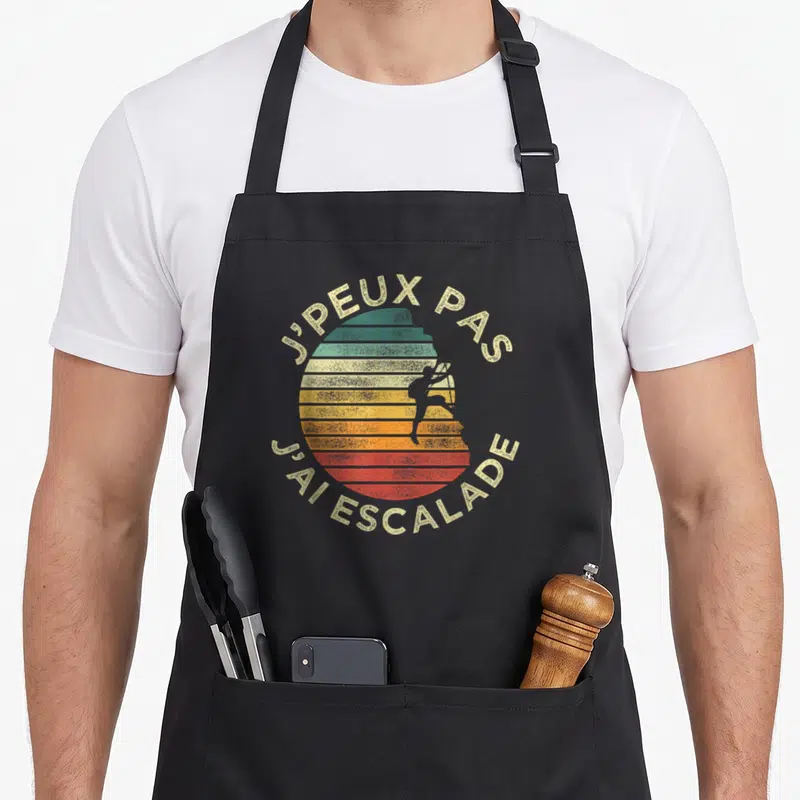 Tablier de cuisine noir avec motif circulaire coloré et silhouette de grimpeur en position d'ascension.