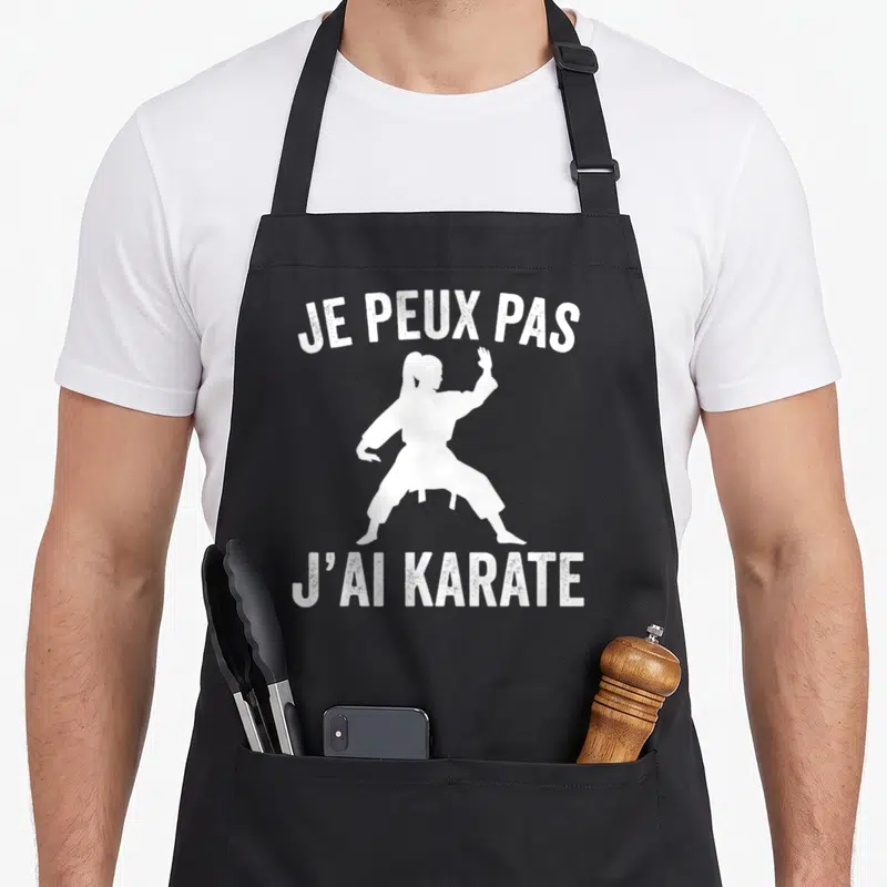 Tablier de cuisine noir avec silhouette blanche d'une femme en karaté et texte humoristique imprimé en haut et en bas.