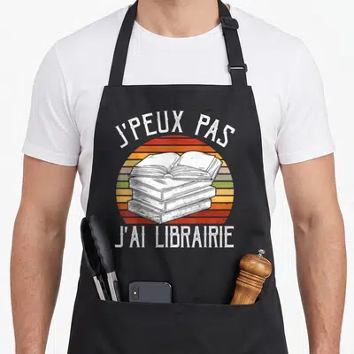 Tablier de cuisine noir avec illustration vintage d'une pile de livres ouverte et texte blanc.