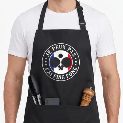 Tablier de cuisine noir avec logo rond blanc, deux paddles croisés et texte je peux pas j'ai ping pong.