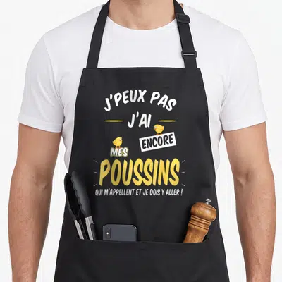 Tablier de cuisine noir avec l'inscription j'peux pas j'ai mes poussins accompagnée de deux illustrations de poussins jaunes.