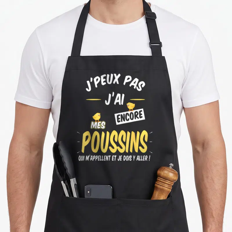 Tablier de cuisine noir avec l'inscription j'peux pas j'ai mes poussins accompagnée de deux illustrations de poussins jaunes.