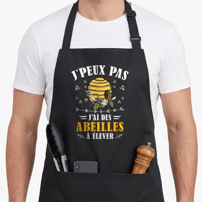 Tablier de cuisine noir avec une ruche jaune, des abeilles et le texte J'peux pas j'ai des abeilles à élever