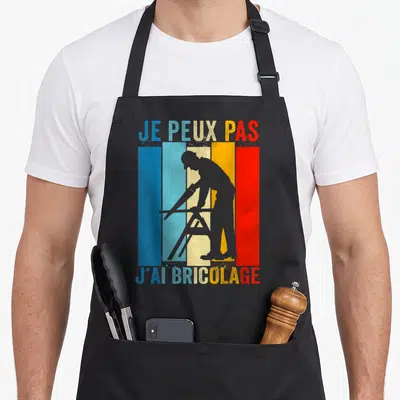 Tablier de cuisine noir avec silhouette de carpenter et texte Je peux pas j'ai bricolage sur fond de bandes colorées.
